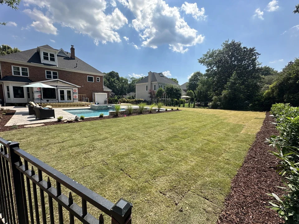 New sod and freshly mulched planting beds surrounding a poolside backyard